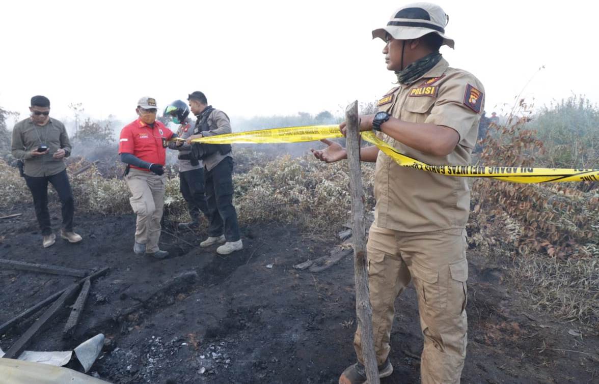 Anggota kepolisian saat memasang garis polisi di lahan yang terbakar