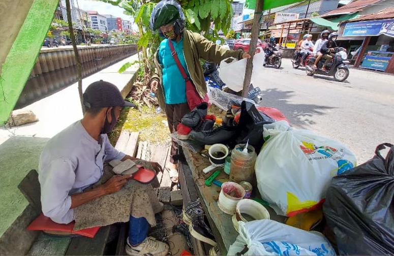 Ujang sedang melayani pelanggannya mengesol sepatu yang telah digelutinya puluhan tahun.